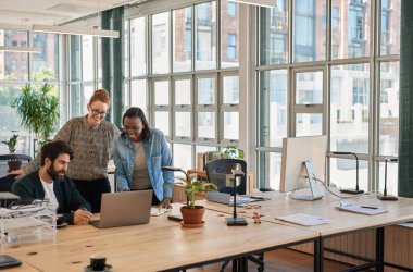 Modern bir ofiste masa başında çalışırken bilgisayarla konuşan bir grup gülen genç iş adamı.