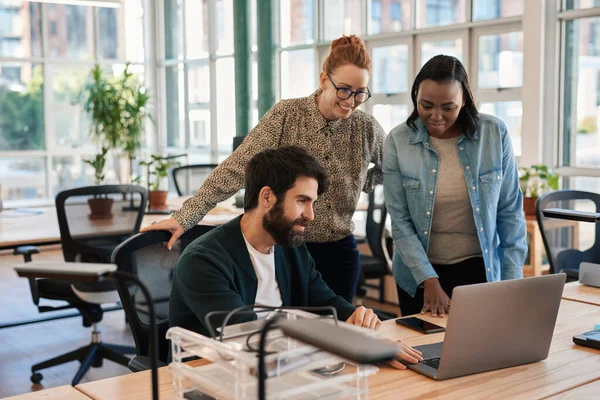在现代化的办公室里 一群面带微笑的年轻人一边在笔记本电脑前聊天 一边在办公桌前工作 — 图库照片