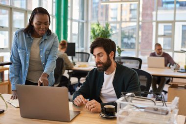 Modern bir ofiste masa başında çalışırken laptopla konuşan iki farklı genç iş adamı.