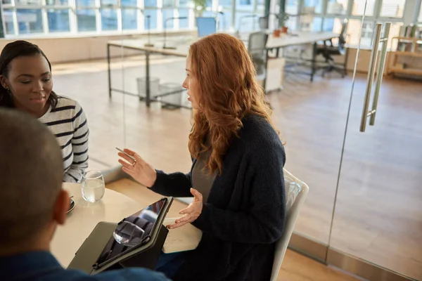 現代的なオフィススペースでコーヒーを飲みながら会議中に多様な同僚のグループのためのタブレットプレゼンテーションを行う若いビジネスマンの女性 — ストック写真