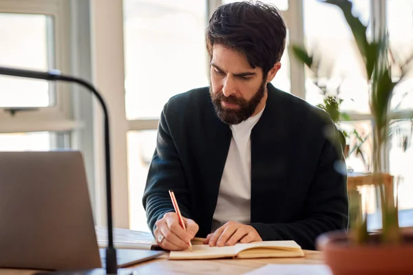 Joven Empresario Enfocado Escribiendo Notas Libro Mientras Trabaja Portátil Escritorio — Foto de Stock