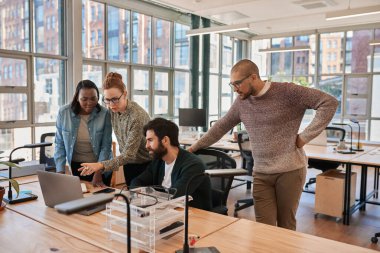 Modern bir ofisteki bir masada dizüstü bilgisayarla çalışan çeşitli odaklanmış genç iş adamları.