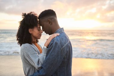 Loving young multiethnic couple standing in each other arms with their eyes closed on a sandy beach at sunset