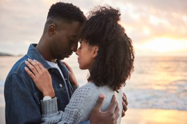 Affectionate young multiethnic couple standing face to face with their eyes closed in each other's arms on a beach at sunset