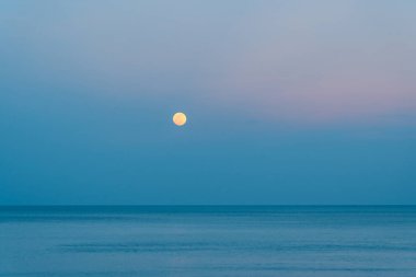 Dolunay rengarenk bir günbatımında denizin üzerinde yükseliyor.