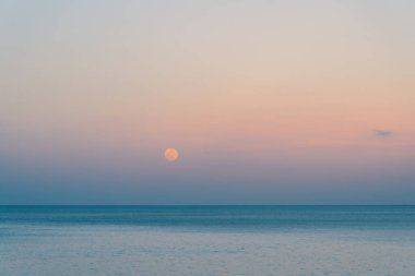 Dolunay rengarenk bir günbatımında denizin üzerinde yükseliyor.
