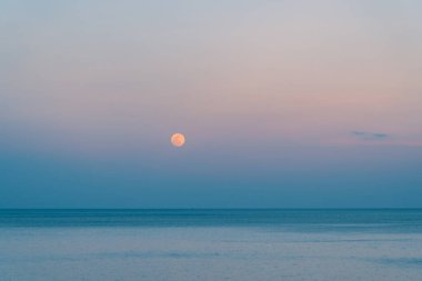 Dolunay rengarenk bir günbatımında denizin üzerinde yükseliyor.
