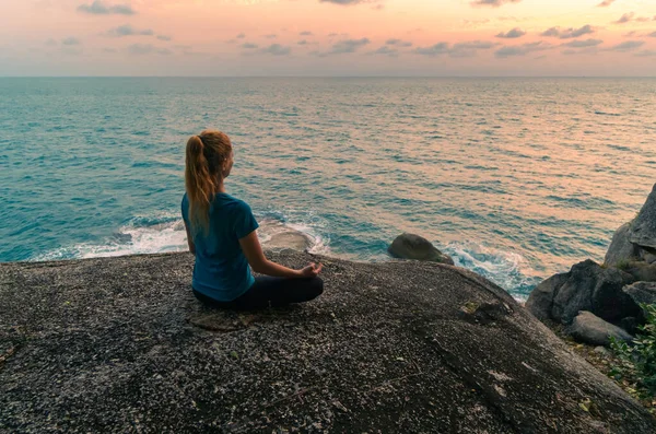 日出日落时 荷花的年轻女子在海边的岩石上沉思 背景是多彩的天空 — 图库照片