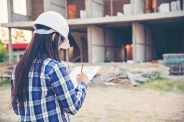 Kadın inşaat mühendisi not yazarken ekose gömlekli beyaz kasketli şantiye işçisi. Mimari Kadın Tasarımı Mühendis İnşaat Kurumu Gayrimenkul