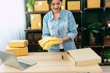 Kadın paket kutusunu masaya koydu. Müşteriye mal teslimatını kontrol ediyor. Asyalı bir kadın ofis masasında küçük bir iş kuruyor. Girişimci Asyalı kadın teslimat için ürün topluyor
