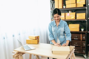 Kadın paket kutusunu masaya koydu. Müşteriye mal teslimatını kontrol ediyor. Asyalı bir kadın ofis masasında küçük bir iş kuruyor. Girişimci Asyalı kadın teslimat için ürün topluyor