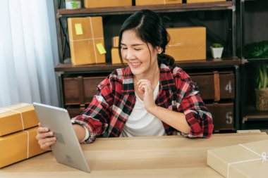 Asyalı bir kadın ev ofisinde küçük bir iş kuruyor. Çevrimiçi satıcı girişimci genç Asyalı kadın çevrimiçi tablet kontrolü kullanıyor. Tablet kullanan kadın stok malları teslimat paketini kontrol et