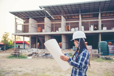 İnşaat mühendisi kadın işçi sanayisinde ekose gömlekli, beyaz kasketli, inşaat işçisi. Mimari mühendis kadın memur emlak projesine bakıyor.