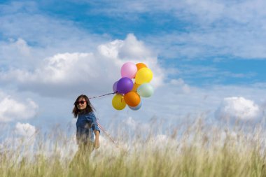 Yeşil çayır üzerinde koşan balonlar tutan neşeli şirin kız beyaz bulut ve mutlulukla mavi gökyüzü. Hava balonları tutan eller doğum günü partisinde oynar. Mutlu zamanlar yaz mevsimi açık havada.