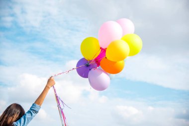 Yeşil çayır bulutu üzerinde koşan balonları tutan bir kadın. Mavi gökyüzü. Mutluluk dolu ve rahatlatıcı. Hava balonları tutan eller doğum günü partisinde oynar Mutlu zamanlar yaz güneşi açık havada