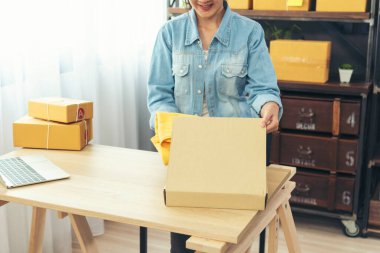 Kadın paket kutusunu masaya koydu. Müşteriye mal teslimatını kontrol ediyor. Asyalı bir kadın ofis masasında küçük bir iş kuruyor. Girişimci Asyalı kadın teslimat için ürün topluyor