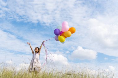 Yeşil çayır üzerinde koşan balonlar tutan neşeli şirin kız beyaz bulut ve mutlulukla mavi gökyüzü. Hava balonları tutan eller doğum günü partisinde oynar. Mutlu zamanlar yaz mevsimi açık havada.