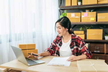 Stok malları teslimat paketlerini kontrol eden bir kadın. Asyalı bir kadın ev ofisinde küçük bir iş kuruyor. Çevrimiçi girişimci Asyalı kadın çevrimiçi kontrol tableti kullanıyor