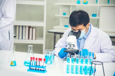 Bilim adamı bilim laboratuarındaki mikroskop araştırmalarını inceliyor. Asyalı bilim adamı laboratuvar kimya laboratuvarlarını arıyor. Covid-19 Coronavirus biyokimya araştırma deneyi aşı konsepti
