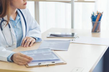 Kadın doktorların eli kapalı reçeteli tıp laboratuarı hastanesi yazıyorlar. Ekinci Asyalı kadınlar klinikte çalışan doktorlara röntgen filmi çektiriyorlar. Not defterine steteskop yazan bir doktor.
