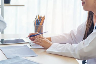 Kadın doktorların eli kapalı reçeteli tıp laboratuarı hastanesi yazıyorlar. Ekinci Asyalı kadınlar klinikte çalışan doktorlara röntgen filmi çektiriyorlar. Not defterine steteskop yazan bir doktor.