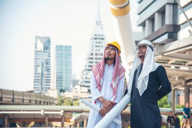 Arap inşaat mühendisi inşaat projesi modern müslüman BAE şehrini işaret ederek projeyi elinde tutuyor. Çok kültürlü iş adamları akıllı mühendislik zekası. Mühendis Konsepti.