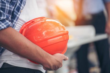 İnşaat mühendisi elleri inşaat mühendisliği için beyaz kaskı tutuyor. İnşaat mühendisi takım elbiseli adam inşaat sahasında beyaz kasklı kaskı elinde tutuyor.