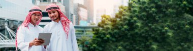 Banner Arab takımı dijital tabletleri sendika çalışanları olarak tutuyor. Akıllı tablet kullanan Panorama Arap grubu modern Müslüman BAE şehrini tartışıyor. Asyalılar kopya alanı ile toplantı yapan takımlara gülümsüyor.