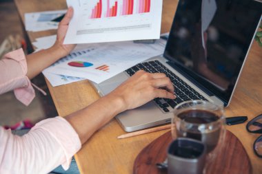 Finans grafikleri okuyan iş kadını pazarlama verilerini analiz etmeyi planlıyor. Akıllı telefon kullanan kadın elleri, ofis masasında dizüstü bilgisayar. Ofiste çalışan Asyalı genç bir kadının elleri..