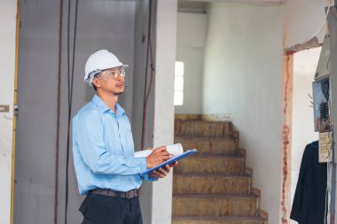 İnşaat mühendisi not yazıyor. İnşaat alanında mavi gömlekli güvenlik kasketi takıyor. Endüstriyel işçi erkek işçi. Mimarcı, mühendis, sivil konstrüksiyon gayrimenkul çiziyor.