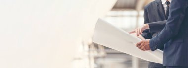 Banner İnşaat Mühendisi Bina planında mavi gömlekli güvenlik önlüğü giyer inşaat sahasındaki fabrikada beyaz şapka giyer. Panorama Mimarlık erkek inşaat mühendisi kopya alanı ile planlara bakıyor.