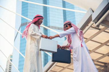 Arap iş adamı müslüman elbisesi modern şehir BAE arka planında el sıkışıyor. Müslüman Erkekler Takım Çalışması İş Ortağıyla Ortaklık tokalaşması. çok ırklı Arap halkı bağlılığa güvenir