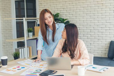 Finansal grafik grafiklerini okuyan iki Asyalı kadın pazarlama verilerini analiz etmeyi planlıyor. Asyalı takım çalışanı ofis firması. Şirket masasında dizüstü bilgisayarla iki iş kadını buluşması..