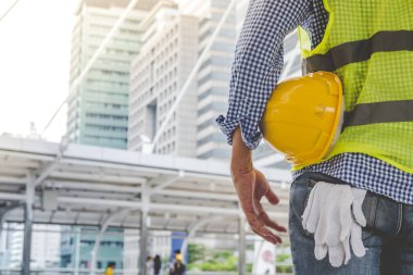 İnşaat mühendisi elleri inşaat mühendisliği için beyaz kaskı tutuyor. İnşaat mühendisi takım elbiseli adam inşaat sahasında beyaz kasklı kaskı elinde tutuyor.