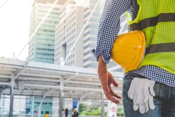 İnşaat mühendisi elleri inşaat mühendisliği için beyaz kaskı tutuyor. İnşaat mühendisi takım elbiseli adam inşaat sahasında beyaz kasklı kaskı elinde tutuyor.