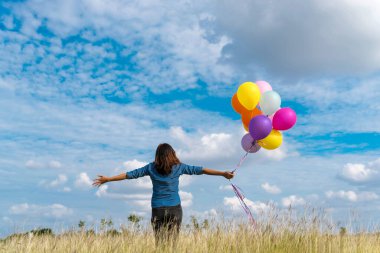 Yeşil çayır üzerinde koşan balonlar tutan neşeli şirin kız beyaz bulut ve mutlulukla mavi gökyüzü. Hava balonları tutan eller doğum günü partisinde oynar. Mutlu zamanlar yaz mevsimi açık havada.