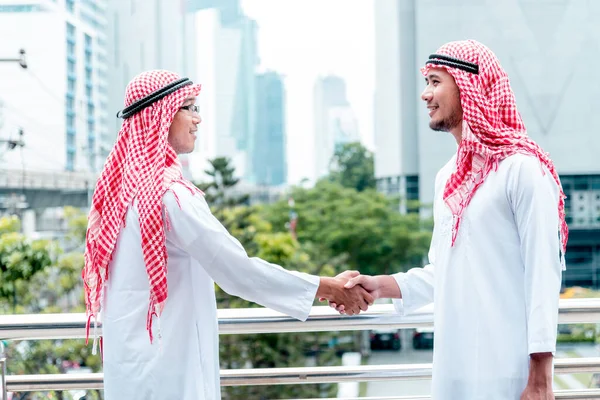 Arab Businessman Muslim dress shaking hands together in modern city UAE background. Muslim Men Teamwork business partner handshake with Partnership. diversity multiracial arab people trust commitment