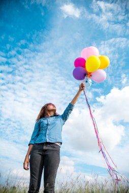 Yeşil çayır bulutu üzerinde koşan balonları tutan bir kadın. Mavi gökyüzü. Mutluluk dolu ve rahatlatıcı. Hava balonları tutan eller doğum günü partisinde oynar Mutlu zamanlar yaz güneşi açık havada