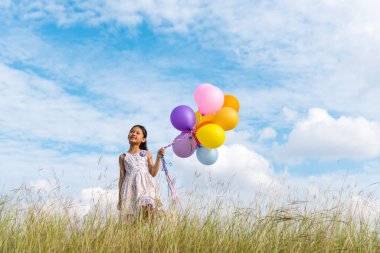 Yeşil çayır üzerinde koşan balonlar tutan neşeli şirin kız beyaz bulut ve mutlulukla mavi gökyüzü. Hava balonları tutan eller doğum günü partisinde oynar. Mutlu zamanlar yaz mevsimi açık havada.