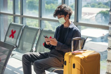 Asyalı genç gezgin, normal yüzlü, sosyal mesafeli, uçağın dinlenme odasında akıllı telefon tutan normal bir adam. Yeni normal erkek yolcu salgını uçakla geliyor. Coronavirus turizm gezisi