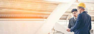 Banner İnşaat Mühendisi Bina planında mavi gömlekli güvenlik önlüğü giyer inşaat sahasındaki fabrikada beyaz şapka giyer. Panorama Mimarlık erkek inşaat mühendisi kopya alanı ile planlara bakıyor.