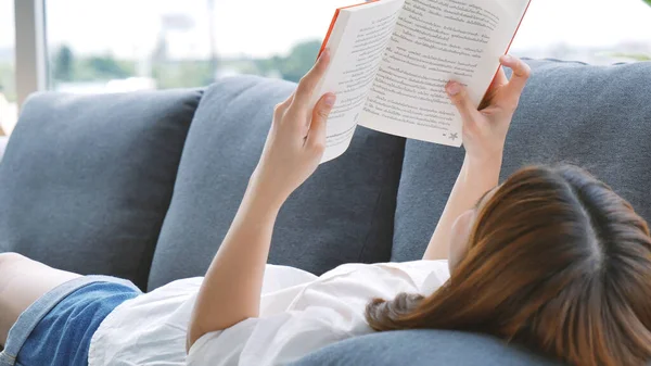 Young asian woman reading book on cozy couch sofa at warm hom. Relax woman holding book read on sofa near window happiness.woman reading open book leisure mind. Happiness woman lifestyle at home