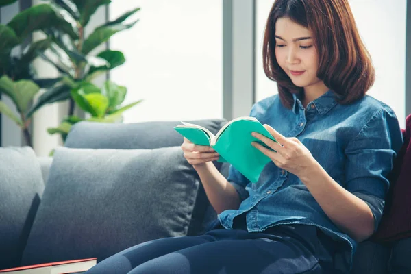 Young asian woman reading book on cozy couch sofa at warm hom. Relax woman holding book read on sofa near window happiness.woman reading open book leisure mind. Happiness woman lifestyle at home