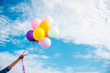Yeşil çayır üzerinde koşan balonlar tutan neşeli şirin kız beyaz bulut ve mutlulukla mavi gökyüzü. Hava balonları tutan eller doğum günü partisinde oynar. Mutlu zamanlar yaz mevsimi açık havada.