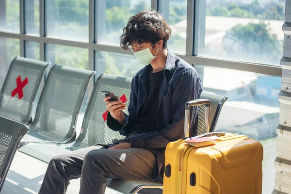 Asian young man traveller new normal holding smartphone in Airplane lounge wear face mask sitting Social distancing. New normal Male travel pandemic passenger by plane. Tourist Men using smartphone