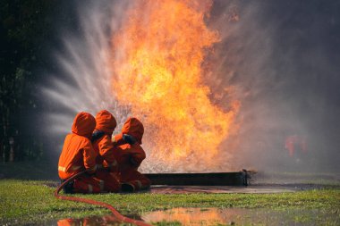 Firefighter Rescue team training in fire fighting extinguisher. Firefighter teamwork fighting with flame using fire hose chemical water foam spray engine. Fireman wear hard hat, safety suit uniform