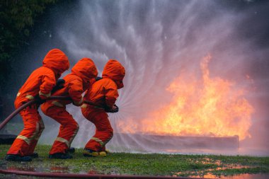 Firefighter Rescue team training in fire fighting extinguisher. Firefighter teamwork fighting with flame using fire hose chemical water foam spray engine. Fireman wear hard hat, safety suit uniform