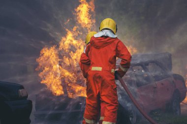 Firefighter Rescue training in fire fighting extinguisher. Firefighter fighting with flame using fire hose chemical water foam spray engine. Fireman wear hard hat, safety suit uniform for protection