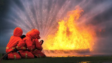 Firefighter Rescue team training in fire fighting extinguisher. Firefighter teamwork fighting with flame using fire hose chemical water foam spray engine. Fireman wear hard hat, safety suit uniform