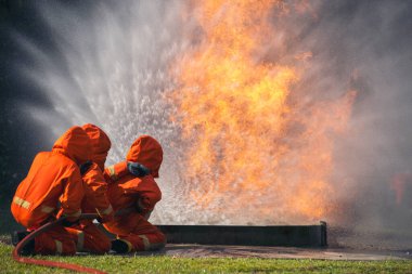 Firefighter Rescue team training in fire fighting extinguisher. Firefighter teamwork fighting with flame using fire hose chemical water foam spray engine. Fireman wear hard hat, safety suit uniform